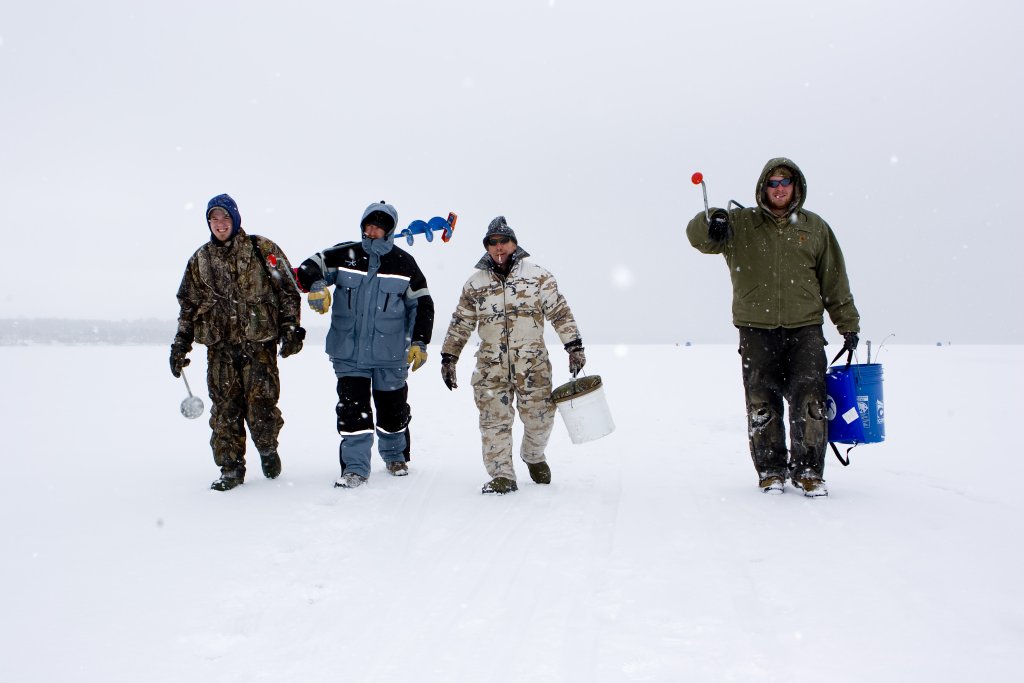 four men in snow gear getting ready to ice fish 