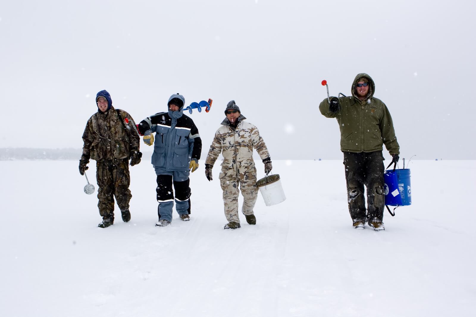 four men in snow gear getting ready to ice fish