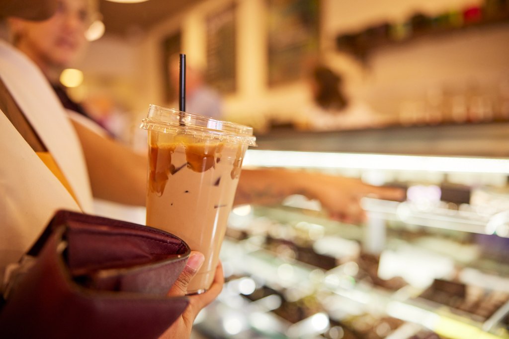 Customer holding an iced beverage looking at a counter case of sweet treats.