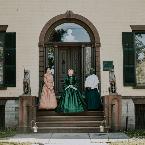 Picture of three women in period dress standing on the steps of the Seward House Museum. These women represent, Frances Seward and Harriet Tubman, famous Underground Railroad Conductor