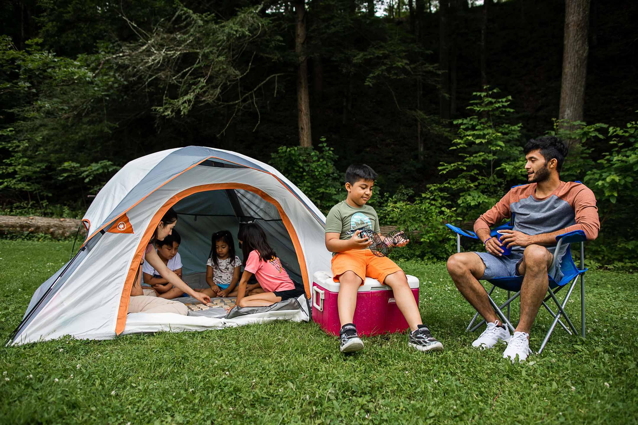 small tent on green grass with family of 2 sitting outside on chairs