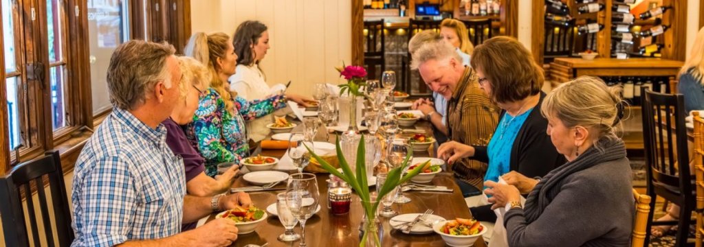 Nine patrons sit at a restaurant table eating salads.