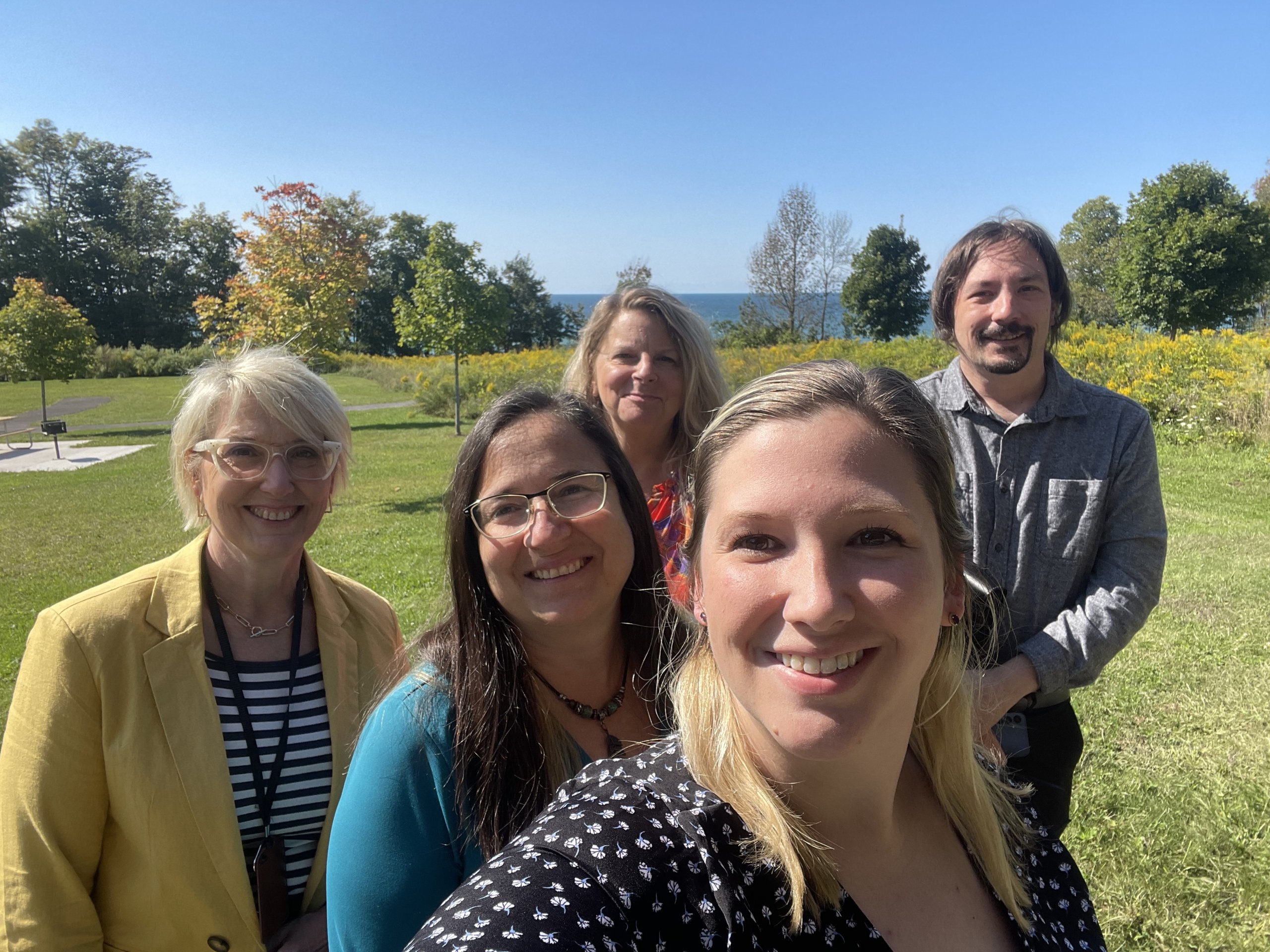 three women and one man standing outdoors during the Sumer with green trees behind them-Tour Cayuga Staff encourages you to contact them to help plan your visit.
