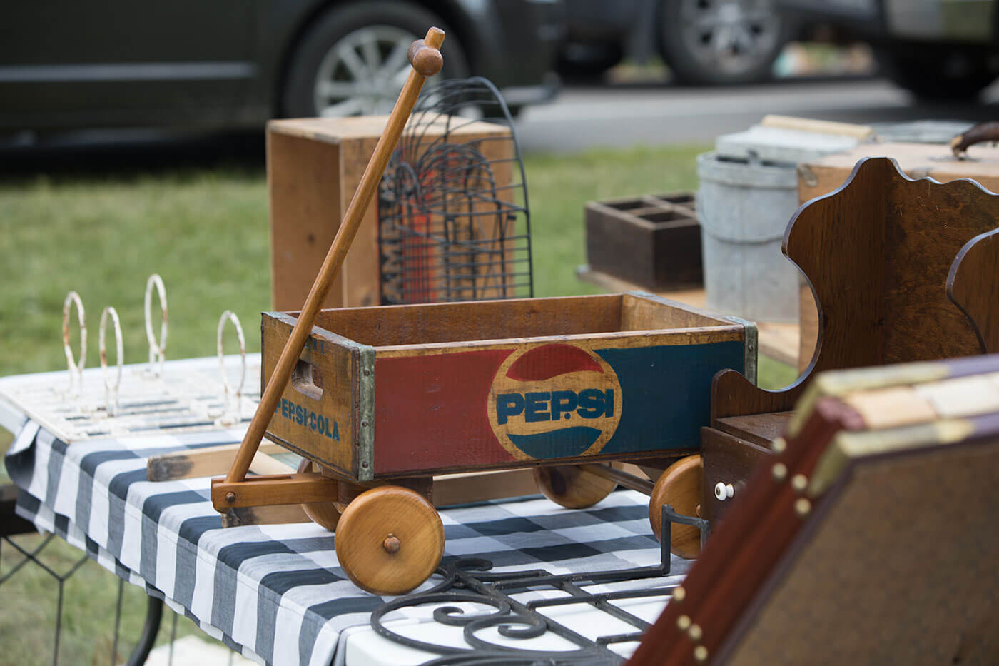 An old wooden wagon with the Pepsi logo painted on it sits on a checkered tablecloth.
