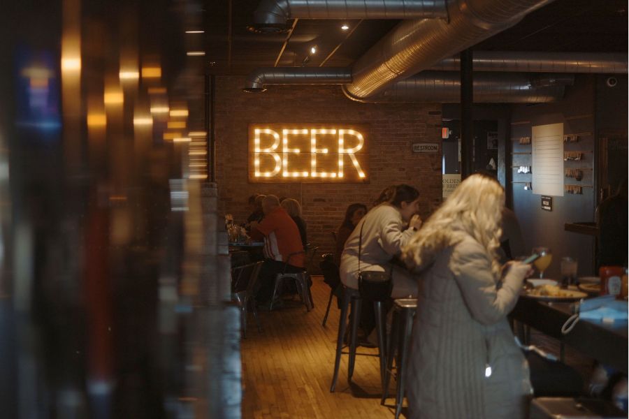 A neon sign that says BEER is in the background of an underground bar with tables of patrons dining.