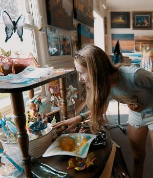 A woman admire pieces are glasswork on a shelf in an art store.